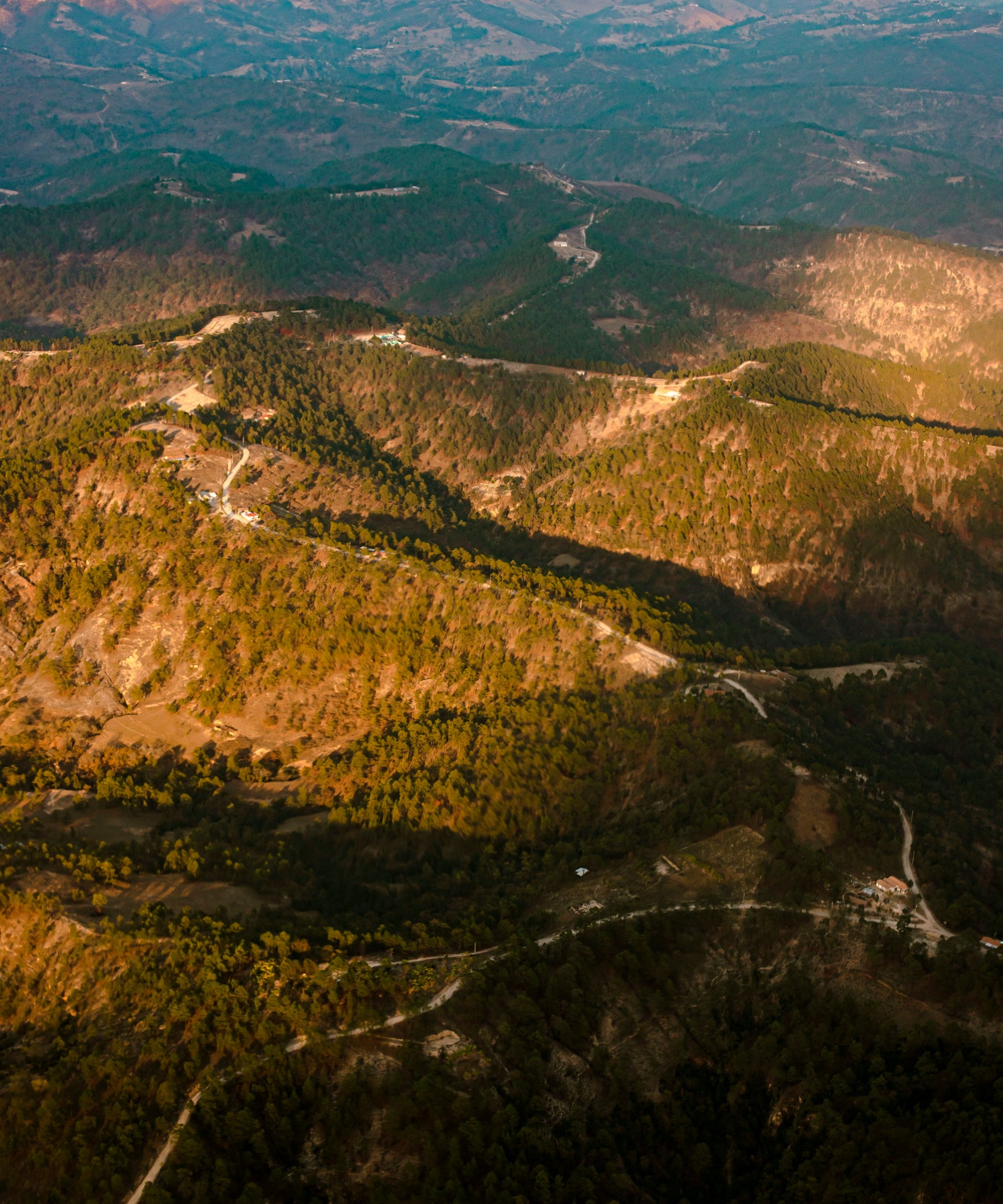 Aerial view of a mountainous landscape with winding roads and greenery.