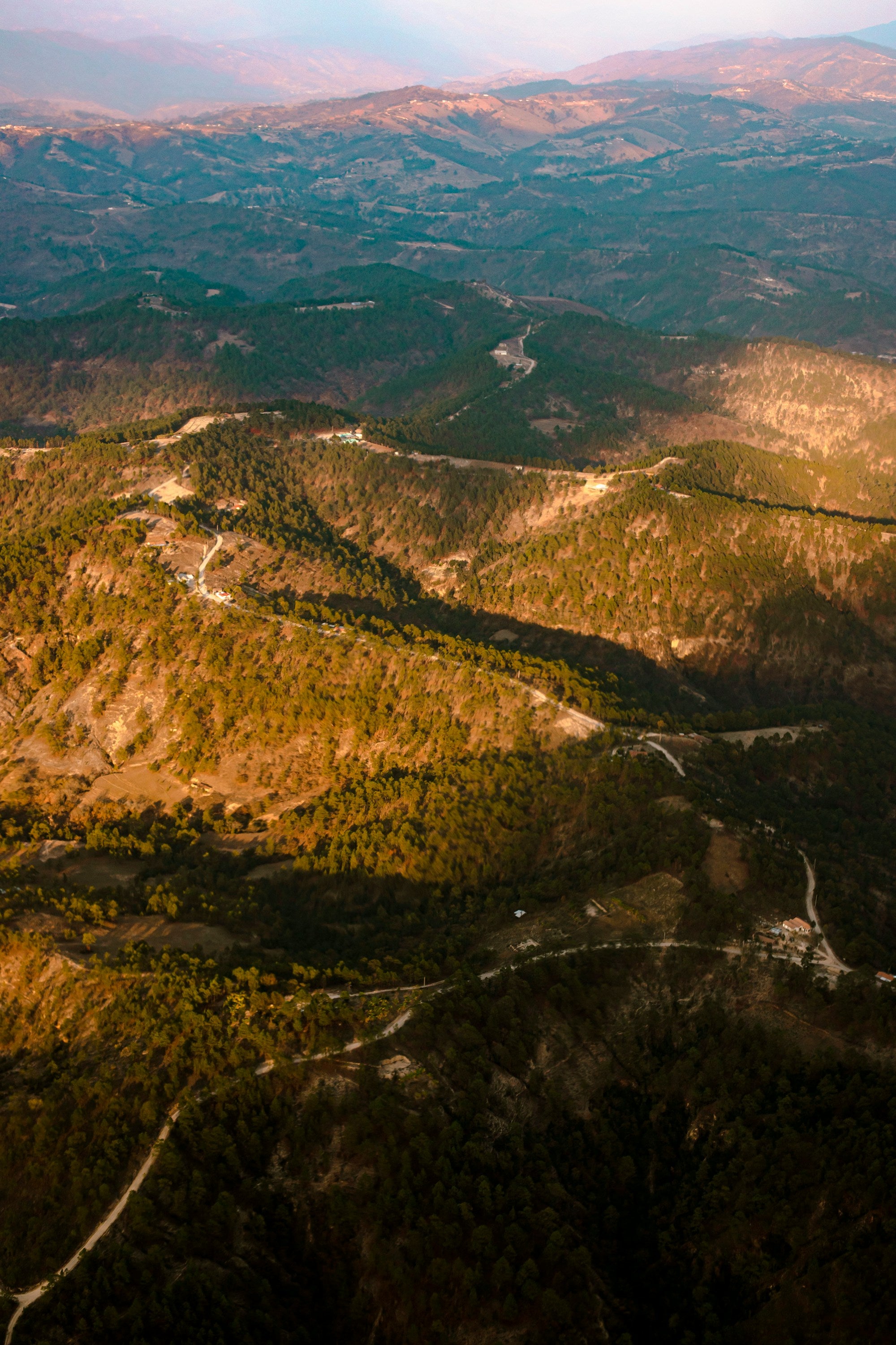 Aerial view of a mountainous landscape with winding roads and greenery.